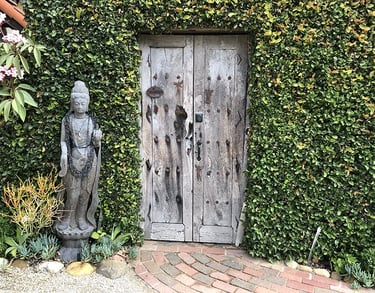 Wood buddha statue by weathered wood gate and vine-covered wall.