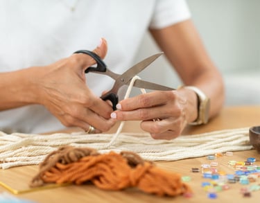 Persona usando tijeras para cortar cordón de algodón en un proyecto artesanal de macramé.