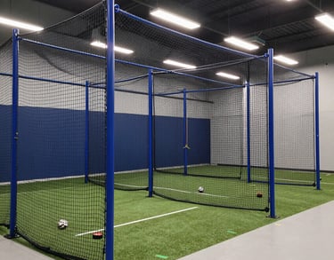 A wide-angle shot of professional indoor batting cages in North American / US, featuring steel blue netting and bright, modern white lighting.