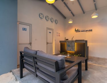 Modern Madi Maldives resort reception desk with lounge seating, world clocks, and ambient lighting.