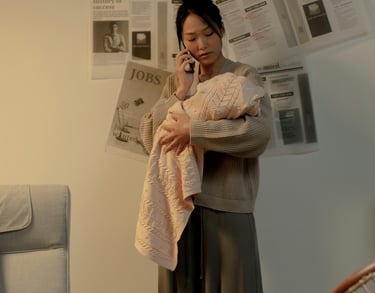 a woman in a sweater holding a baby and talking on a cell phone