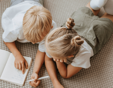 two kids laying on floor and writing