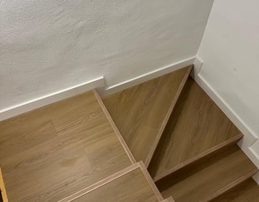 Escalera de madera, tonos claros, pared blanca.