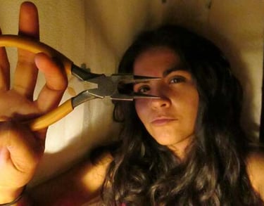 En una habitación con poca luz, una mujer sostiene un par de alicates amarillos de punta larga 