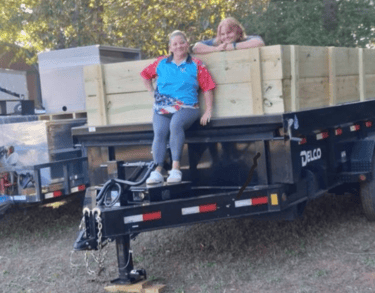 Owner, Sherieanne Skinner and daughter, Lily, standing up on her dump trailer