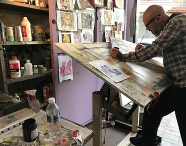 O artista em pé diante de uma tela, com uma expressão pensativa, enquanto decide o próximo mo