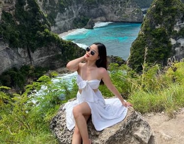 A woman in a white dress posing at Diamond Beach viewpoint in Nusa Penida, Bali.