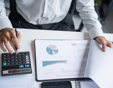 Person analyzing financial reports with calculator and charts
