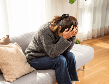 a woman sitting on a couch with her hands on her head