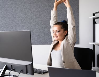 a woman sitting at a desk with her arms up in the air stretching