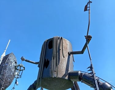 A large rustic metal sculpture of a mechanical character with a lantern and staff against a clear blue sky.