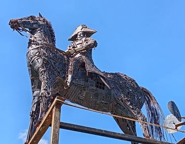 A metal scrap sculpture of an equestrian statue of Napoléon against a clear blue sky.
