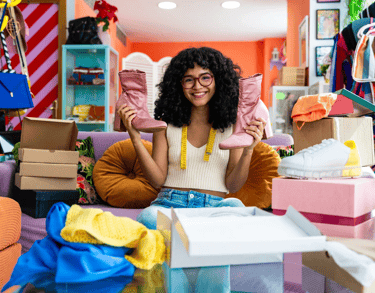 a woman sitting on a couch in a room with boxes of clothes