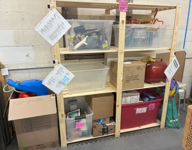 Wooden shelf with clear tubs, boxes, and red tubs filled with donations. 