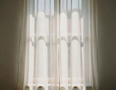 Abstract shot of sunlight through a sheer curtain in a Spanish-speaking interior, creating soft patterns on an off-white wall, evoking serenity and light.