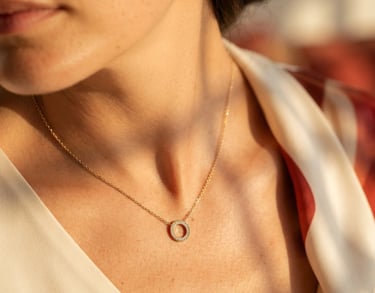 Macro close-up of a delicate stainless steel gold-plated necklace resting on a woman's collarbone, warm direct sunlight casting soft architectural shadows, cream background, high-end editorial photography.