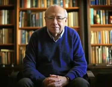 a man in a blue sweater and black pants sitting in front of a bookshel
