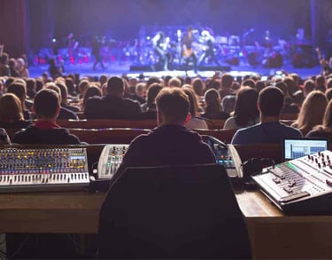 Live event technician operating multiple audio mixers during a stage performance, representing Sonus' technical support servi