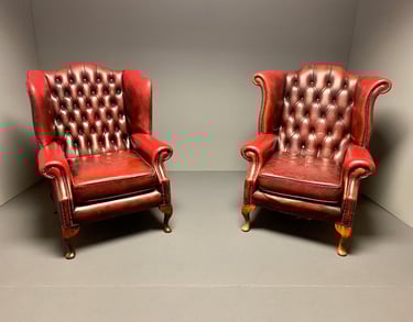 Two vintage, orang leather armchairs with tufted backs sit side by side in a minimalist, neutral-colored room. 