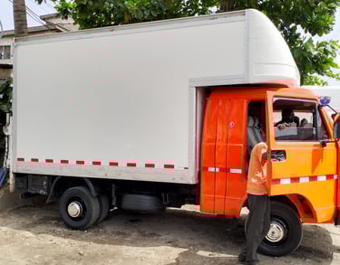 An orange cab delivery truck with a white enclosed cargo box and red reflective stripes, parked on a