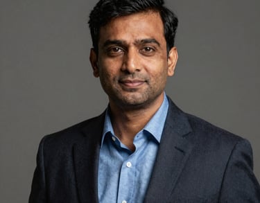 Professional studio portrait of a South Asian male executive in his 40s, wearing a steel blue shirt and dark blazer, neutral background.