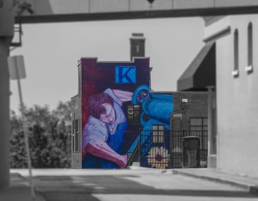 Urban mural of a labor figure on the Kansan Building, with selective color against a grayscale streetscape.