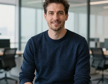 A professional headshot of a male career advisor in a dark blue sweater, sitting in a bright modern office with glass partitions.