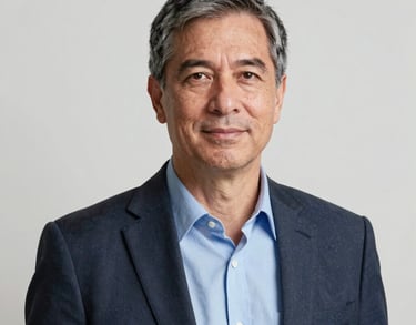 A professional headshot of a male senior coach in business casual attire, standing in front of a clean white wall with soft, flattering lighting.
