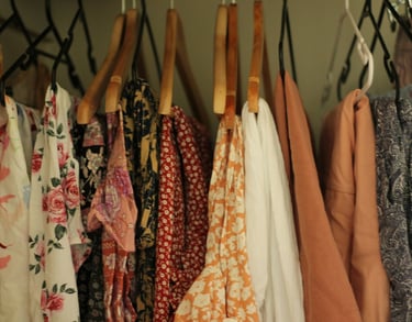 vestidos florales y prendas estampadas colgadas en ganchos de madera y plástico dentro de un clóset.