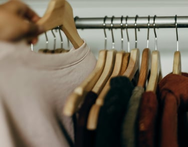 Una mano seleccionando un suéter rosa de un perchero con ganchos de madera para organizar el clóset.