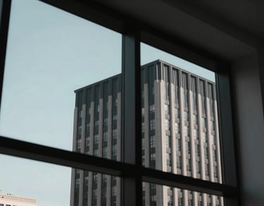 A view through a modern window in a North American / US city, showing the clean lines of professional architecture with a charcoal black and muted light blue sky background.