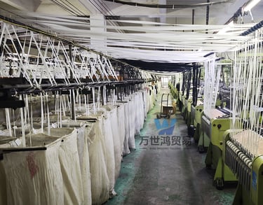 Industrial textile machinery in a zipper manufacturing plant is weaving white fabric yarn.