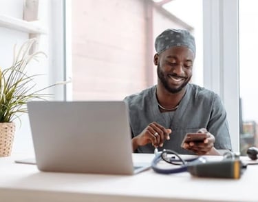 a pharmacy man sitting at a desk with a laptop and a cell phone