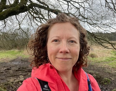 photo of Iona Reading, Health Coach in red jacket standing in front of a tree smiling