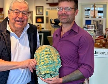 Picture of artist Matt Heft holding a USCGC Barque Eagle custom plaque with Thames River Gallery owner. John Johnson