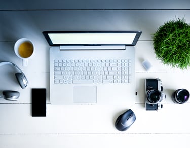 mesa-com-computador-fone-de-ouvido-café-câmera-celular-e-uma-planta-em-cima