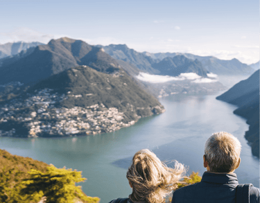 a couple of people sitting on a bench looking at the view of a lake