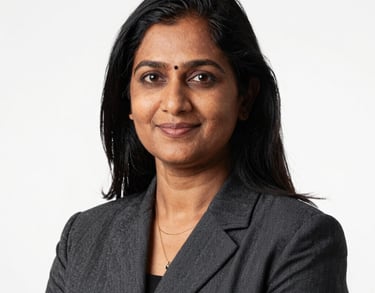 A professional studio portrait of a South Asian female educator in professional attire. She has a warm, intelligent expression. Clean, high-key lighting against a white background.