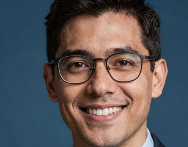 Close-up headshot of a younger professional male with glasses, smiling, professional studio lighting with a steel blue background, South American / Brazilian appearance.