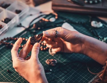 Manos de artesana sosteniendo una piedra preciosa mientras crea joyería hecha a mano.