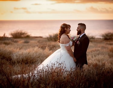 Mariés se regardant au coucher de soleil, robe épaules dénudées et costume noir, face à la mer. mer.