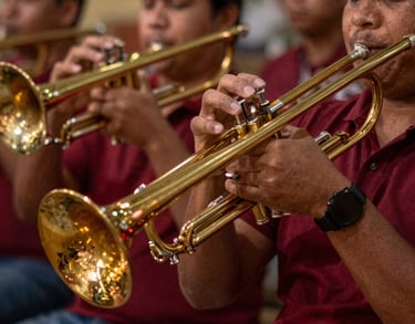 A close-up South American / Brazilian Amazonian musical photography shot. Dynamic, warm-lit capture of hands playing brass instruments like trombones and trumpets, reflecting gold and deep carmine red festive lights.