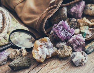 Cristales en bruto de amatista morada y ágata derramados de una bolsa de lona, junto a una lupa