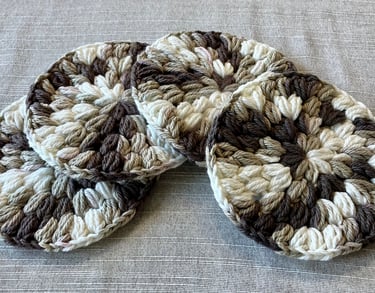 4 brown, tan, and cream crocheted drink coasters lying in a row.