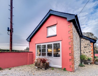 A charming pink rendered cottage with stone walls and large windows in a rural setting.