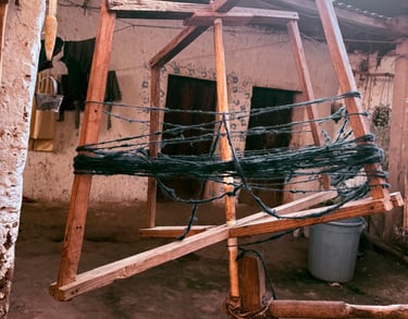Devanador tradicional de madera enrollando hilo de lana oscura en un patio rústico al aire libre.