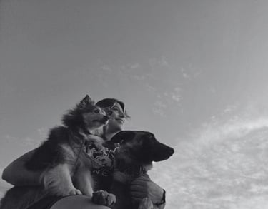 Mujer sonriendo mientras agraza a sus dos perros en un evento de educación canina 