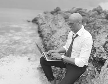 « Bruno Valery travaillant sur son ordinateur, assis sur un rocher les pieds dans l’eau en Guadeloupe »
