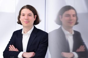 Ein Mann im Anzug steht vor seiner Spiegelung in einer Glasscheibe