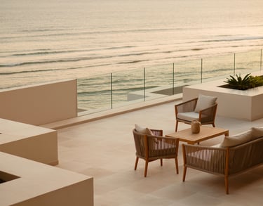 Luxury outdoor patio furniture set on a modern stone terrace with sunset ocean views.